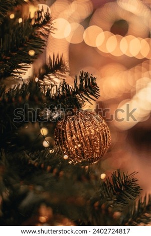 Gold Christmas ball hanging on a Christmas tree with golden garland lights. Decorated spruce branches.