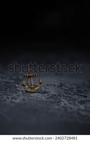 Metallic anchor close up on abstract black background. necklace of small bronze anchor. symbol of sailors, reliability, confidence. naval, pirates, travel concept. element for design.