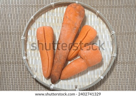 Four damaged substandard carrots on a bamboo colander Royalty-Free Stock Photo #2402741329