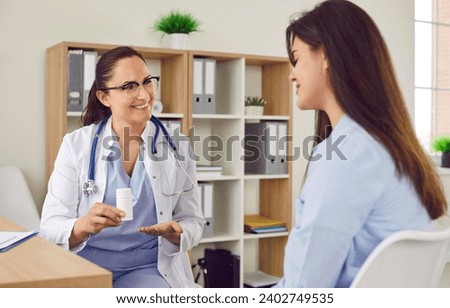 Young female doctor sitting on her workplace at the desk in doctor's office prescribing treatment to a young sick woman patient giving her pills after medical exam. Health care concept.