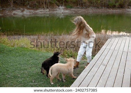 Cute blond girl, 7-years-old having fun on the pier of the pond. The kid dress on boots, delicate shades of clothes, sweater and jeans