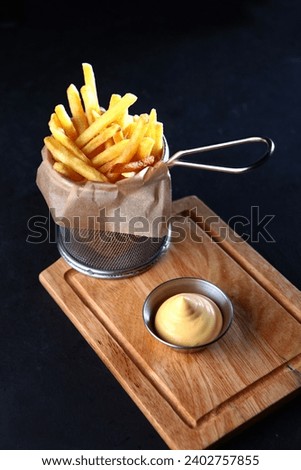 French fries in metal wire basket with sauce on dark background. Fried potatoes. Concept of fast food and junk foo. Vertical photo.