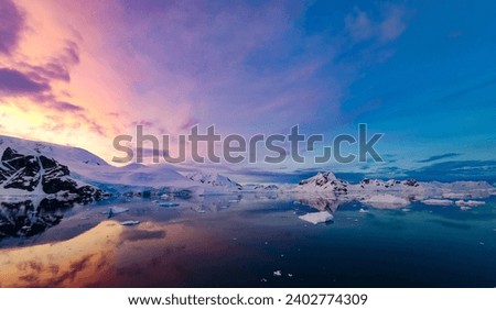 Stunning sunrise in Antarctica with glaciers and mountains reflecting in the prefectly still water.  Royalty-Free Stock Photo #2402774309