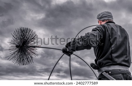 A chimney sweeper on the rooftop of a house checking a smoking chimney. Illustrative editorial. Royalty-Free Stock Photo #2402777589