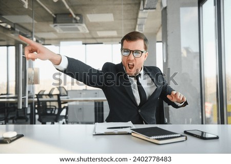 Angry senior businessman sitting at his desk and screaming. Royalty-Free Stock Photo #2402778483