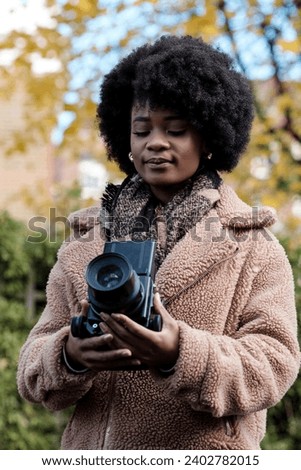 Curly black woman enjoying his photography hobby using a medium format camera. She is looking at waist level finder. It is a cold autumn winter day and she is wearing a thick winter coat and scarf.