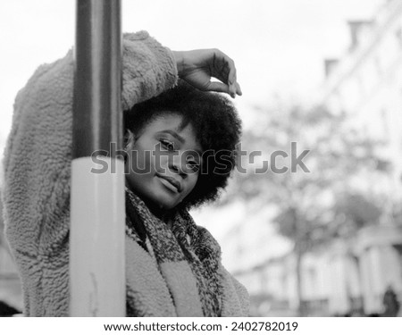 Confident young black woman leaning on bar with a proud attitude. She is looking straight to camera and she is wearing winter outfits. Image made with analog medium format camera.