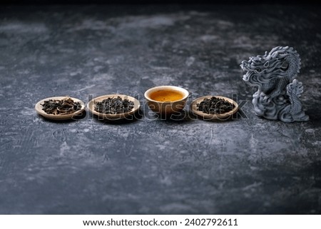 dragon figurine, clay teacup and plate with different sort of tea leaves on dark background. Asian culture cuisine concept. tea ceremony in Japanese or chinese style