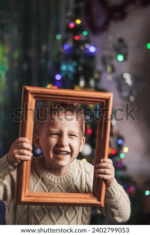 portrait of a cute boy of European appearance in a wooden picture frame against the backdrop of a Christmas tree in the room