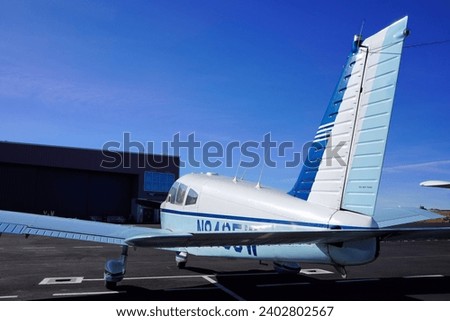 Rear View of a Small White and Blue Airplane in Front of a Hangar Royalty-Free Stock Photo #2402802567