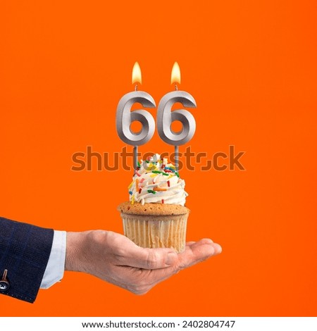 The hand that delivers cupcake with the number 66 candle - Birthday on orange background Royalty-Free Stock Photo #2402804747