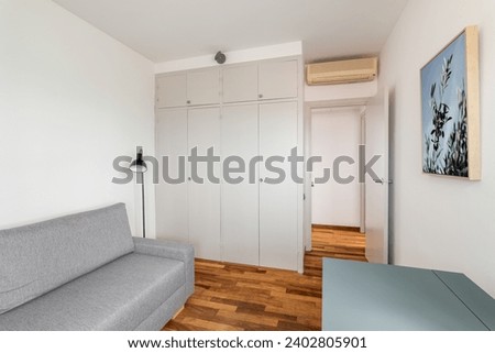 Large wardrobe, grey sofa and desk in elegant empty room