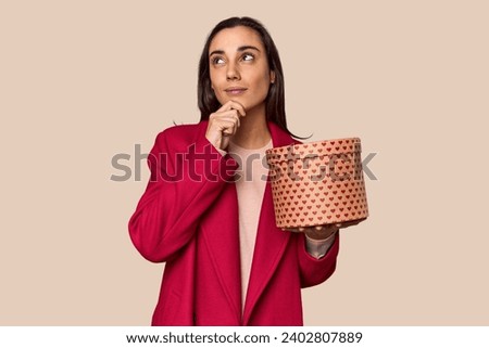 Caucasian woman with Valentine's gift box looking sideways with doubtful and skeptical expression.