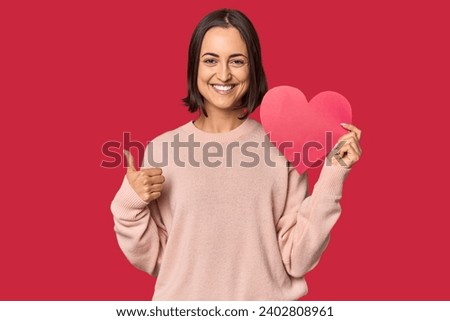 Young woman holding Valentine's heart smiling and raising thumb up