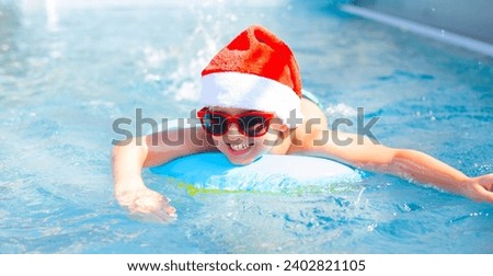 Child boy in a red santa hat and sunglasses swims in a colorful rainbow inflatable circle in the pool
