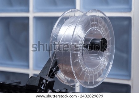 A roll of white transparent high quality 3D printing filament mounted on a modern 3D printer device, closeup. Consumer grade thermoplastic materials used for object product prototyping and design Royalty-Free Stock Photo #2402829899