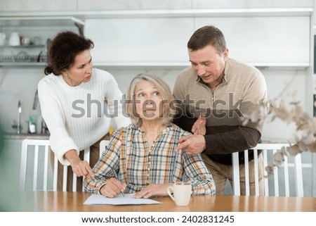 Middle-aged family members partitioning inheritance with mother sitting at kitchen-table with a sheet of paper and pen in hand Royalty-Free Stock Photo #2402831245
