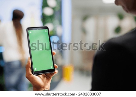 Customer using smartphone with green screen to check apparel reviews before buying clothes. African american woman holding mobile phone with chroma key display in shopping center