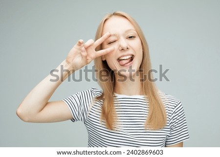 Portrait of a pretty young blond woman showing the peace sign on grey color background
