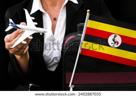 business woman holds toy plane travel bag and flag of Uganda 