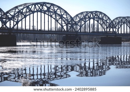 A metal arched bridge across the river with the reflection of the bridge in the water in the form of an arch Royalty-Free Stock Photo #2402895885