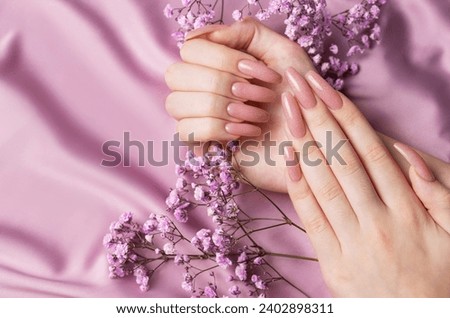 Female hands with beautiful manicure  with gypsofila flowers on pink silk Royalty-Free Stock Photo #2402898311