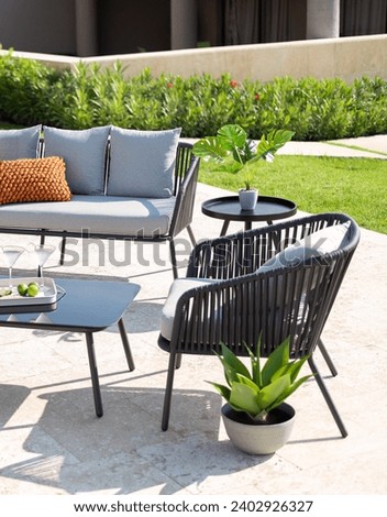 Modern Outdoor Relaxation Space with a Sleek Black Wireframe Sofa and Matching Armchairs with Grey Cushions, a Round Coffee Table, a Snug Potted Snake Plant, on a Terrace Amidst Verdant Shrubbery.