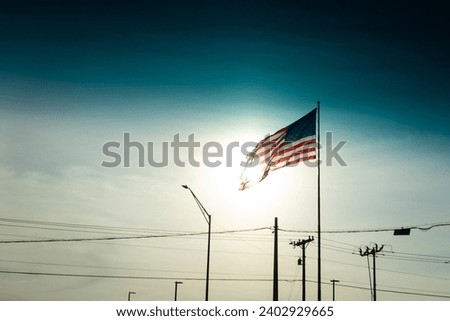 Huge American flag waving in wind over street lamps and power line, usa Royalty-Free Stock Photo #2402929665