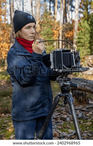Woman taking photo in the forest landscape using large format view camera. Beginner's mistake - dark slide not removed before the exposure.