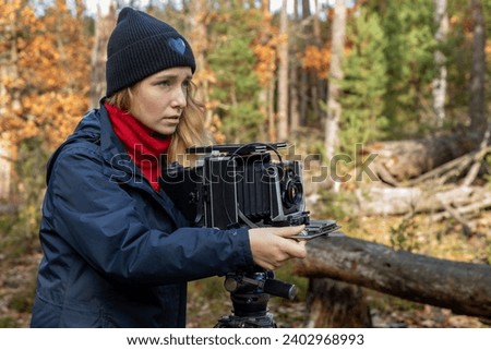 Woman taking photo in the forest landscape using large format view camera. Film holder lies on top of the camera.  