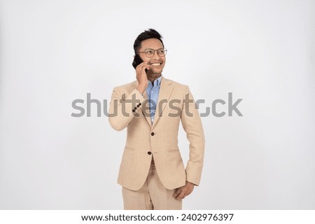 A handsome and professional Asian businessman is talking on the phone with someone, standing on an isolated studio white background. Business people, CEO, manager, boss, business entrepreneur