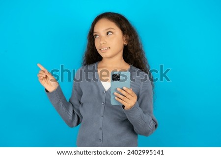 Smiling Young beautiful teen girl holding mobile phone and pointing aside at copyspace.