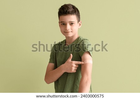 Little boy pointing at plaster after vaccination on green background
