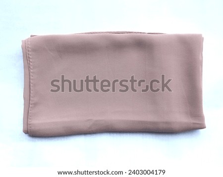 The pashmina hijab worn by Muslim women in dark mocha color is neatly folded on a white background. Royalty-Free Stock Photo #2403004179