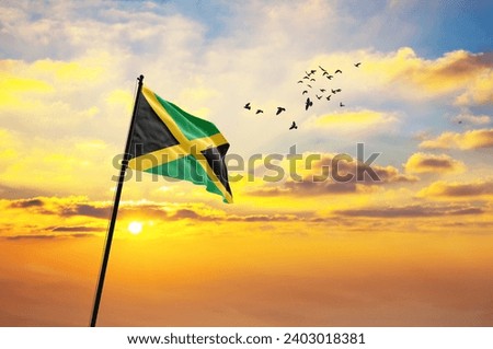 Waving flag of Jamaica against the background of a sunset or sunrise. Jamaica flag for Independence Day. The symbol of the state on wavy fabric.