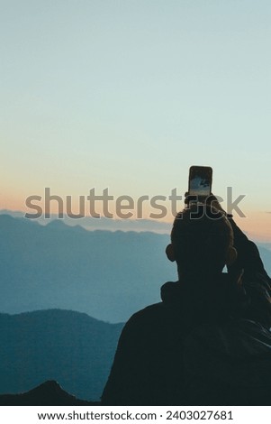 Young male photographer standing and taking photos on the mountain, background view of mountains and clouds, sunset.