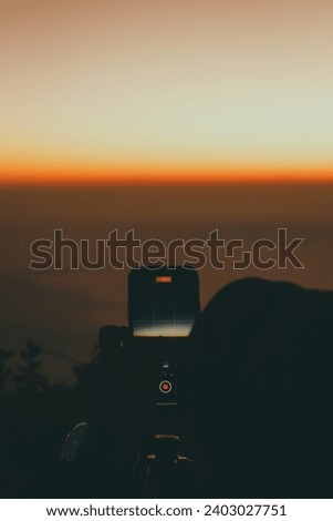 Young male photographer standing and taking photos on the mountain, background view of mountains and clouds, sunset.
