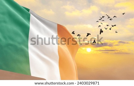 Waving flag of Ireland against the background of a sunset or sunrise. Ireland flag for Independence Day. The symbol of the state on wavy fabric.