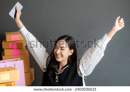 Close-up photo of an Asian female online seller who owns a startup business, smiling, raising her hands in joy. Sales have surpassed the company's target, with many customers ordering products.