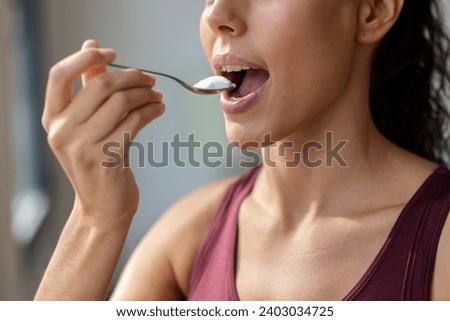 Close up of beautiful sporty woman eating yogurt while looking forwards through the window at home. Royalty-Free Stock Photo #2403034725