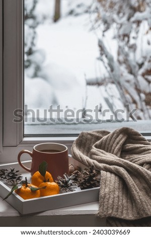 White tray with a mug of coffee and tangerines and a knitted scarf on a winter windowsill. Cozy winter composition. Royalty-Free Stock Photo #2403039669