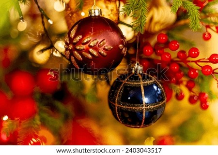 two colorful decorative blue and red balls with golden ornament on fir tree branch of christmas tree, among flashing lights garland