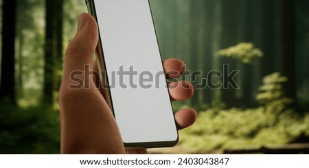 CU Man using his phone outdoors in the forest during hiking or camping trip. Blank screen smartphone mockup, trail, travel, maps, photo application template