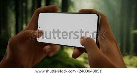 CU Man using his phone outdoors in the forest during hiking or camping trip. Blank screen smartphone mockup, trail, travel, maps, photo application template. Horizontal orientation