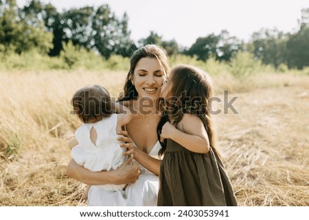 Mother spending time with children outdoors on a summer day. Little girl kissing her mother on cheek.