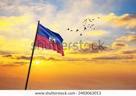 Waving flag of Haiti against the background of a sunset or sunrise. Haiti flag for Independence Day. The symbol of the state on wavy fabric. Royalty-Free Stock Photo #2403063013