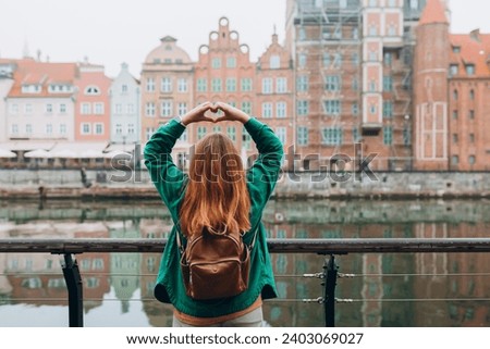 Adventure women making by hands in shape of love heart. Attractive young female tourist is exploring new city. Traveling Europe in autumn, rainy day, rear view