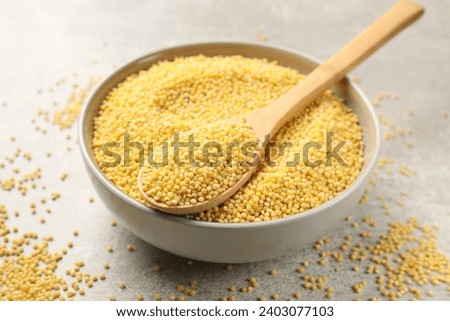 Millet groats in bowl and spoon on light grey table, closeup Royalty-Free Stock Photo #2403077103