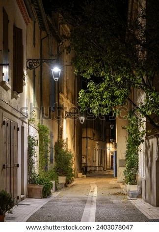 Narrow street in the old part of Arles, France, called La Roquette. Night picture, street lamps, chiaroscuro atmosphere. Translation of the sign : Street Waldeck Rousseau, 1836.