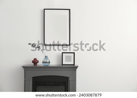 Fireplace, decorative elements and photo frames in room with white wall, space for text. Interior design